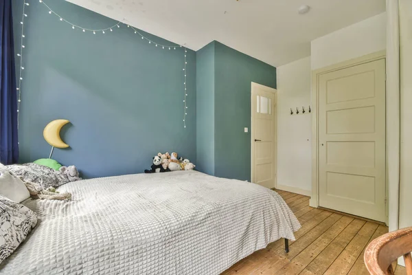 a bedroom with blue walls and white bedding, wooden flooring and string lights hanging from the ceiling above