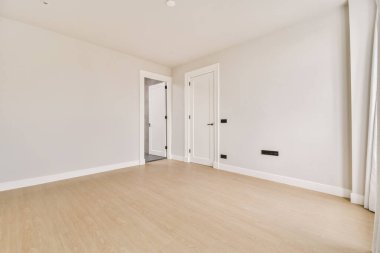 Beyaz duvarları ve sağında ahşap döşemeleri olan boş bir oda. Başka bir odaya açılan bir kapı var.