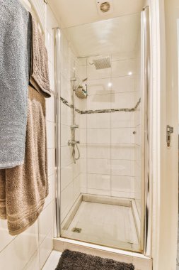 Duvarında havlular asılı bir banyo ve köşesinde cam duş kapısı olan bir havlu askısının yanında.