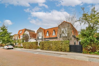 Önlerinde arabaları olan caddenin kenarındaki bazı evler ve yol boyunca büyüyen yeşil çalılar.