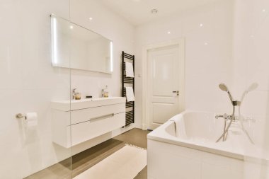 Beyaz duvarları ve ahşap döşemeleri olan modern bir banyo. Köşesinde de serbest bir küvet.