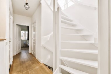 Beyaz bir merdiven, ahşap döşeme ve ahşap tırabzanlar ön kapıdan çekilmiş bir ev içi fotoğrafı.