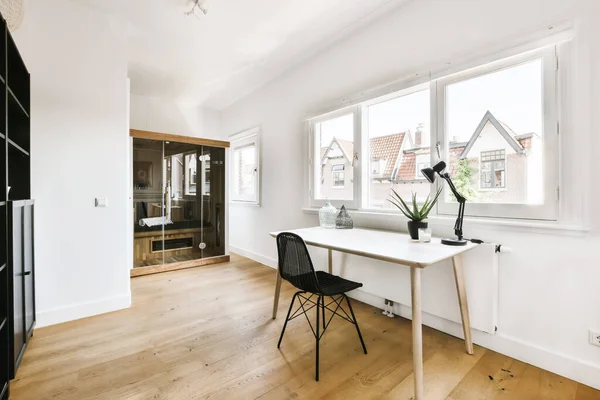 a white room with wood flooring and a desk in front of a window that looks out onto the street