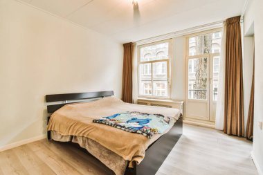 Ahşap döşemeli bir yatak odası ve şehir manzarasına bakan geniş bir pencere.