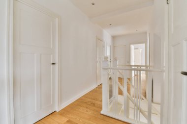 Odanın ortasında beyaz duvarları ve ahşap döşemeleri olan boş bir oda, duvarda bir ayna var.