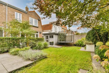 Banliyöde bir ev, evin her iki yanında yeşil çimenler ve çalılar olan küçük bir bahçe var.