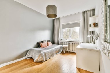 Ahşap döşemeli, açık gri duvarlı, penceresinin etrafında beyaz süslemeli bir yatak odası.