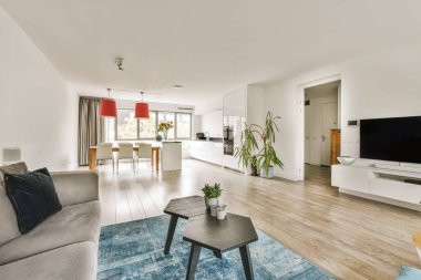 Beyaz duvarları ve ahşap döşemeleri olan bir oturma odası. Ortasında gri bir kanepe ve kahve masası var.