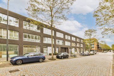 Kenarında arabalar olan bir şehir caddesi ve arka tarafında binalar, hepsi sağa doğru dizilmiş.