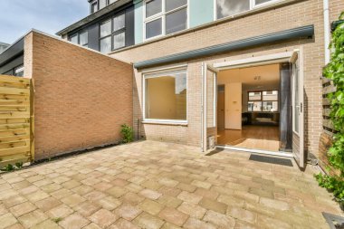 Yeşil sarmaşıklarla çevrili, tuğladan duvarları ve ön kapıya çıkan ahşap merdivenleri olan bir alan.