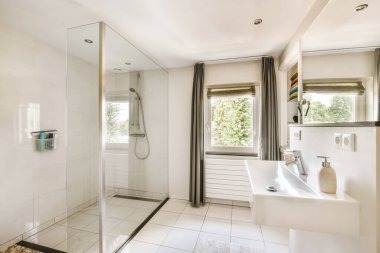 a modern bathroom with white tile flooring and large glass shower stall in the corner of the bathtub is next to the window