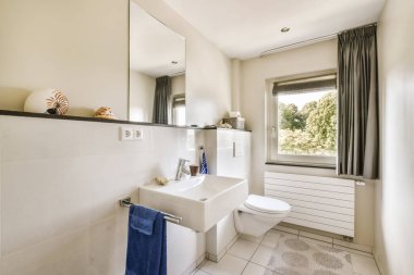 a bathroom with a toilet, sink, and window in the photo is taken to the right there are two towels hanging on the