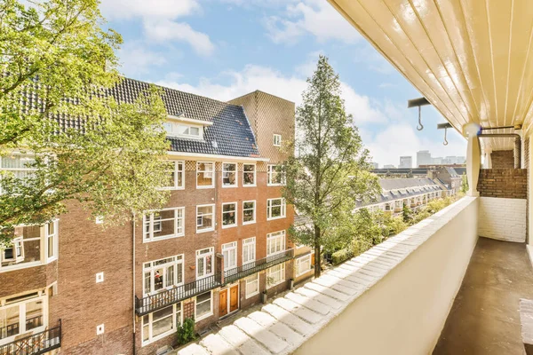 a balcony with trees and buildings in the background, taken from an apartments roof terrace window looking out onto the street