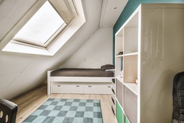 a small room with a bed, desk and books on the floor in front of a window that looks out to the sky