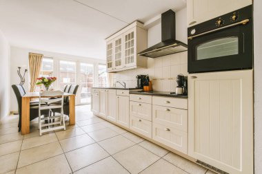 Tezgahında beyaz dolaplar ve siyah aletler olan bir mutfak. Arka planda da da yemek odası var.