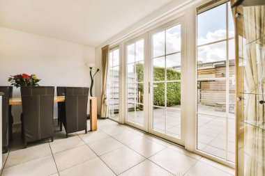 Yerde cam kapılar ve beyaz fayanslar olan bir oturma odası. Önünde bir yemek masası var.