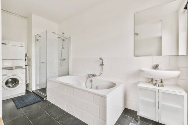 a white bathroom with black tile flooring and a washer in the corner next to the bathtub is on the wall