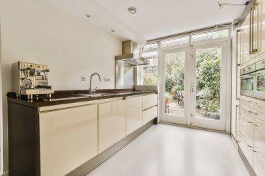 Modern bir mutfak, beyaz dolapları ve siyah tezgahları var. Avluya açılan açık bir doord alanında.