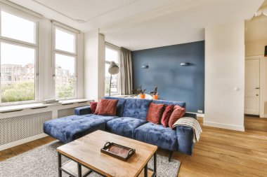 Mavi kanepeleri ve beyaz duvarları olan bir oturma odası. Odanın ortasında ahşap döşeme ve ahşap sehpa.