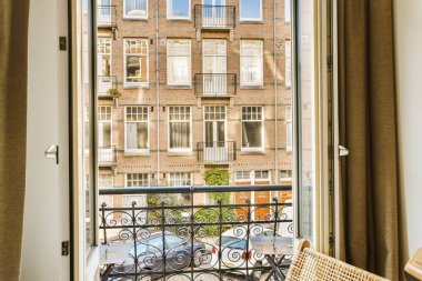 a balcony with a chair and table in front of an open window looking out onto the cityscapea