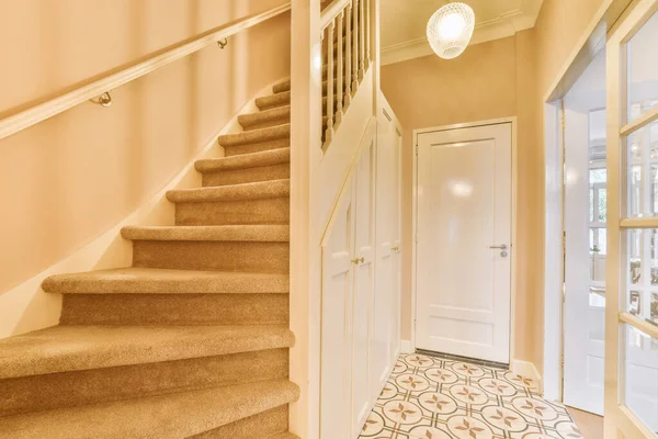 a hallway with carpet and white door handle on the left handrails are in front of the stairs, leading up to the