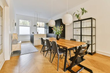 Ahşap döşemeleri ve beyaz duvarları olan bir yemek odası. Ahşap bir masa, siyah sandalyeler ve duvarda bir bitki var.