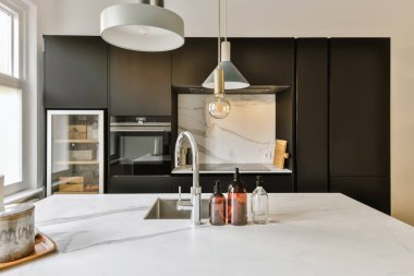 Fotoğrafta beyaz mermer tezgahlı bir mutfak ve siyah dolaplar ön camdan lavaboya kadar çekiliyor.