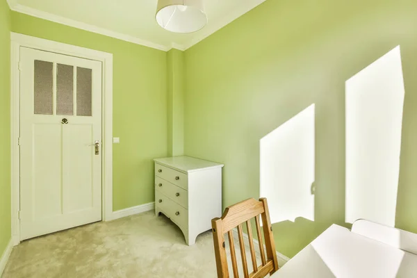 a room with green walls and white trim on the door, window, and chair in front of the room