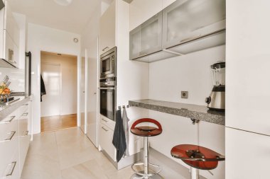 a kitchen area with white cabinets and counters, including a red bar stool in the center of the room