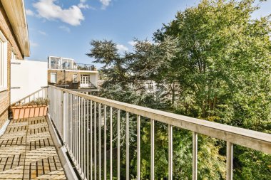 a balcony with white railings and green trees in the fore - image was taken from an apartments roof terrace