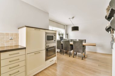 Ahşap döşemeleri, beyaz duvarları ve açık renkli dolapları olan bir evde mutfak ve yemek odası.