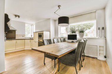 Ahşap zemini ve beyaz duvarları olan bir yemek odası. Odanın ortasında büyük bir masa var.