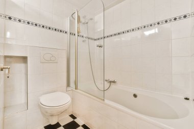 Yerde siyah beyaz fayanslar, duş kabini ve odanın köşesinde tuvalet olan beyaz bir banyo.