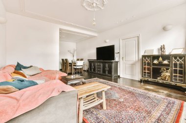 Duvara monte edilmiş bir televizyon setinin önünde pembe kanepeleri ve halıları olan bir oturma odası.