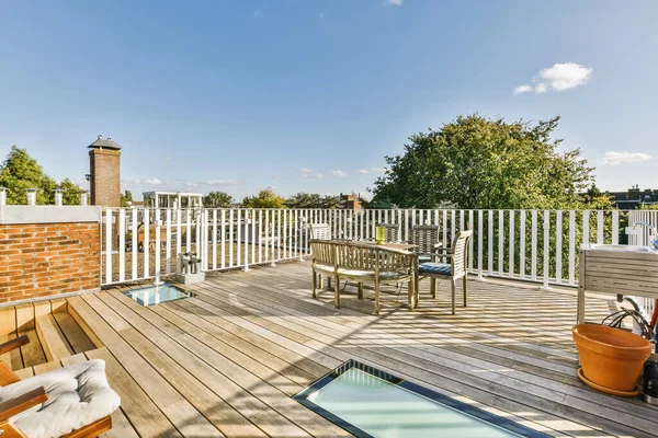 stock image a wooden deck with chairs and an outdoor pool in the middle part of the deck, surrounded by white pickets