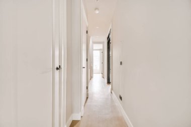 Beyaz duvarları ve yan yana ahşap döşemeleri olan uzun bir koridor diğer odalara açılıyor.