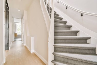 Bir evin merdivenlerinde hafif ahşap döşeme ve merdivenlerin kenarında ikinci kata çıkan beyaz parmaklıklar var.