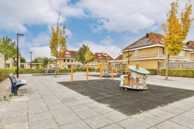 Her iki tarafında sarı ve turuncu ağaçlar, yukarıda mavi gökyüzü olan yerleşim yerinin ortasında boş bir oyun alanı.