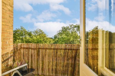 Arka planında ahşap bir çit olan bir dış alan ve odaya ışık girmesi için kısmen kapatılmış bir pencere.