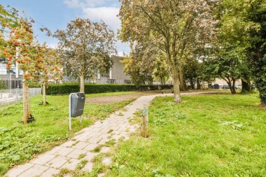 İki tarafında ağaçlar ve çalılar olan yerleşim yerinin ortasında boş bir kaldırım var. Posta kutusu var.