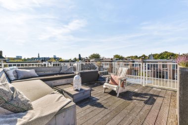 Üst güvertede koltukları, sandalyeleri ve masaları olan bir çatı. Uzaktaki şehrin ufuk çizgisine bakıyor.