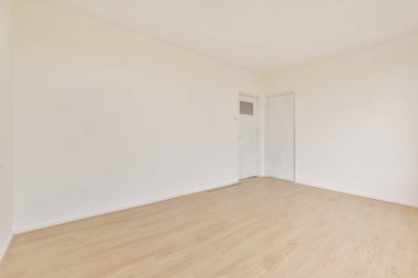 Ahşap zemini ve beyaz duvarları olan boş bir oda. Odanın sol tarafına açılan bir kapı var.