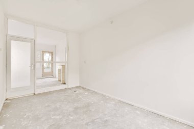 Duvarında beyaz duvarlar ve gri döşeme tahtaları olan boş bir oda. Başka bir odaya açılan bir kapı var.