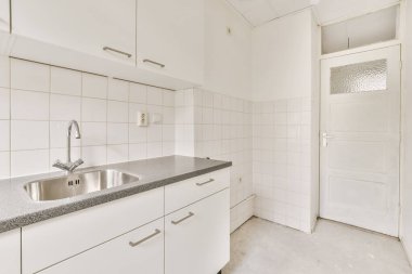 Tezgahın üstünde beyaz dolaplar ve siyah granit tezgahlı bir mutfak var. Bu fotoğrafta sol tarafta.