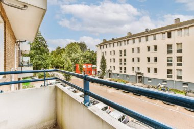 Arka planda mavi korkuluklu bir balkon ve bir apartmanın çatı terasından alınmış binalar.