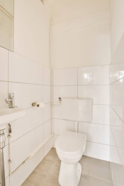 Duvarlarında beyaz fayanslar olan bir banyo ve lavabonun yanındaki tuvalet görünür.