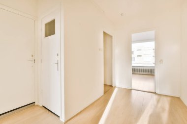 Odanın her iki tarafında beyaz duvarları ve ahşap döşemeleri olan boş bir oda var. Başka bir odaya açılan bir kapı var.