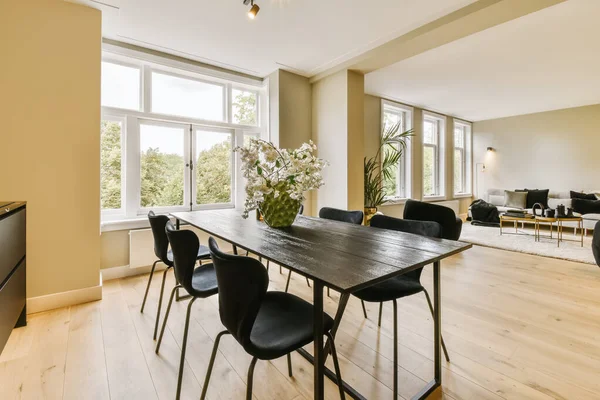 a dining table and chairs in a living room with large windows looking out onto the trees outside on a sunny day