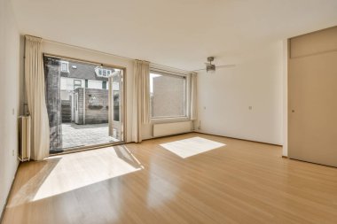 Boş bir oturma odası, ahşap zemin ve bu apartmanın verandasına açılan sürgülü cam kapılı.