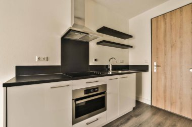 a kitchen with black counter tops and white cupboards, wood flooring and wooden doors in the door is open